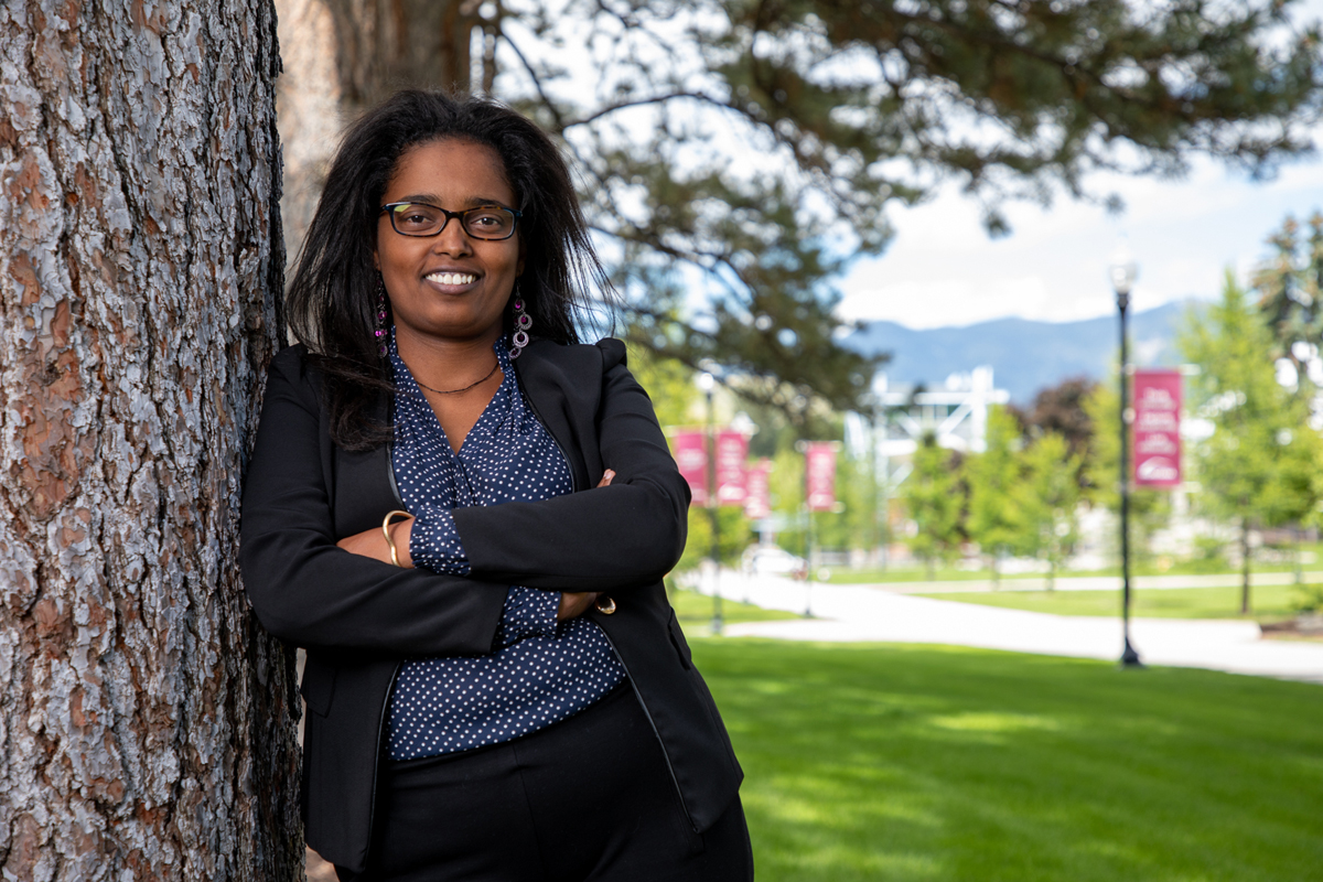 Doctoral student Hana Meshesha leans against a tree outside the Education Building and smiles at the camera.