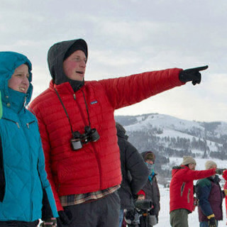 outside on a snowy, winter day, a university of montana graduate student in winter clothing points to the distance while other students look on