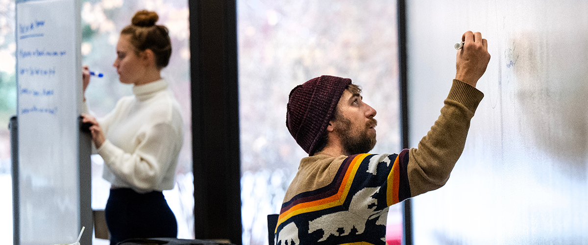 a university of montana student sitting and writing on a mobile whiteboard wall