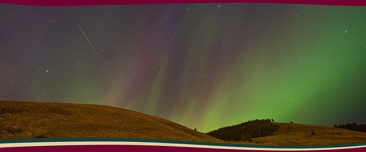 The northern lights illuminate the night sky over the mountains near the UM campus